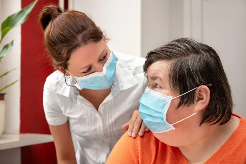 Disabled woman and her support worker in facemasks while looking at each other