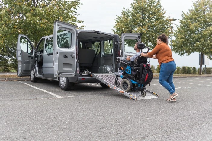 Support worker assisting disabled man in wheelchair to get inside the van