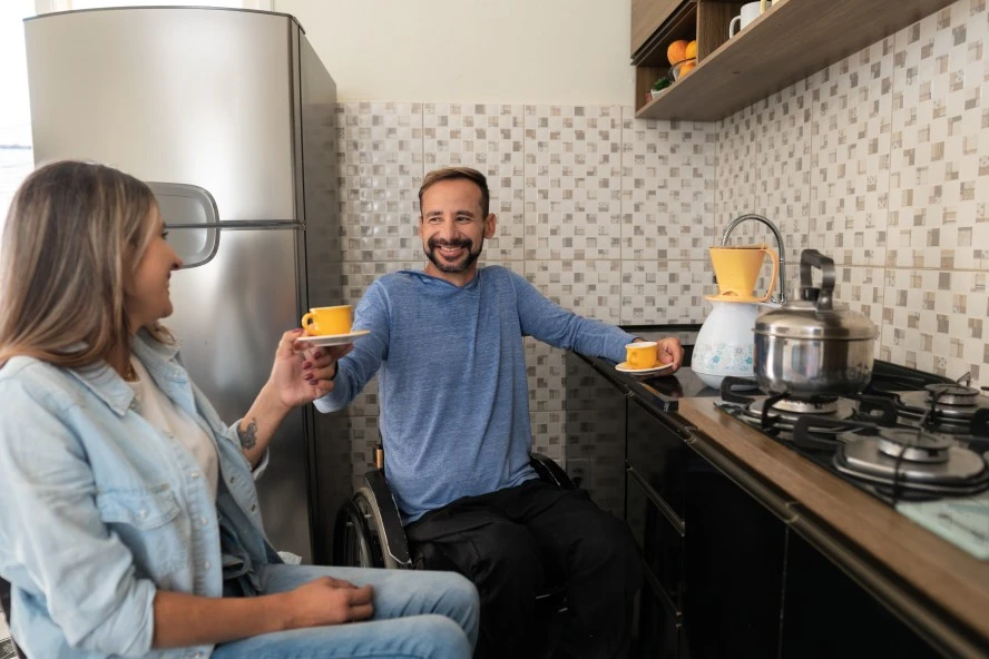 Disabled man in wheelchair passing cup of tea to friend